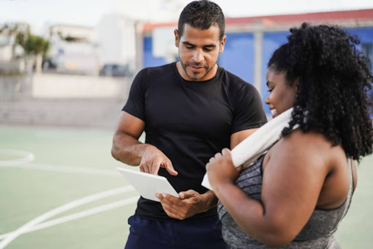 Coach discussing training plan with athlete on a sports court using a digital tablet