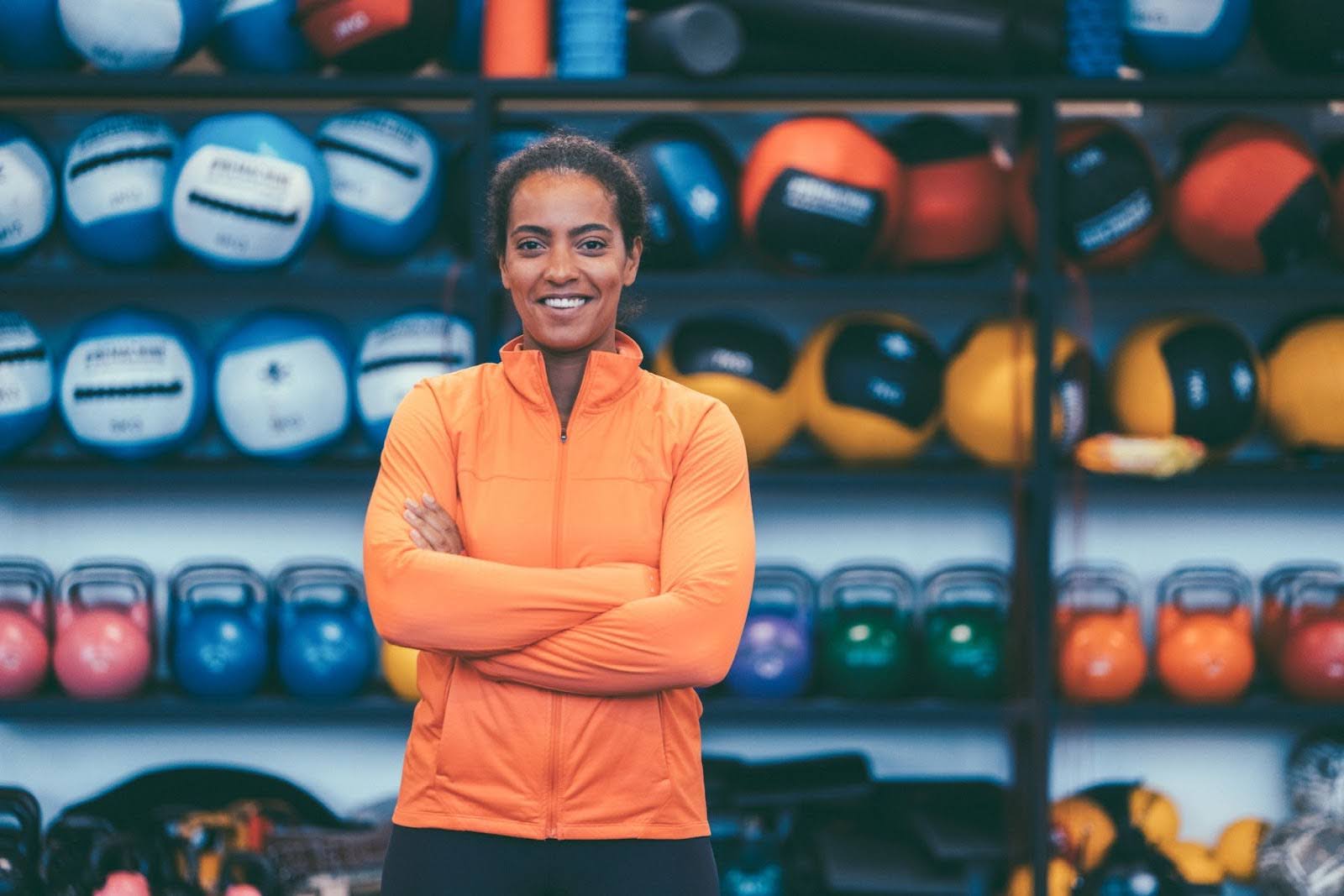 Smiling female sports nutrition expert standing confidently in front of kettlebells, symbolizing success in fitness and career development