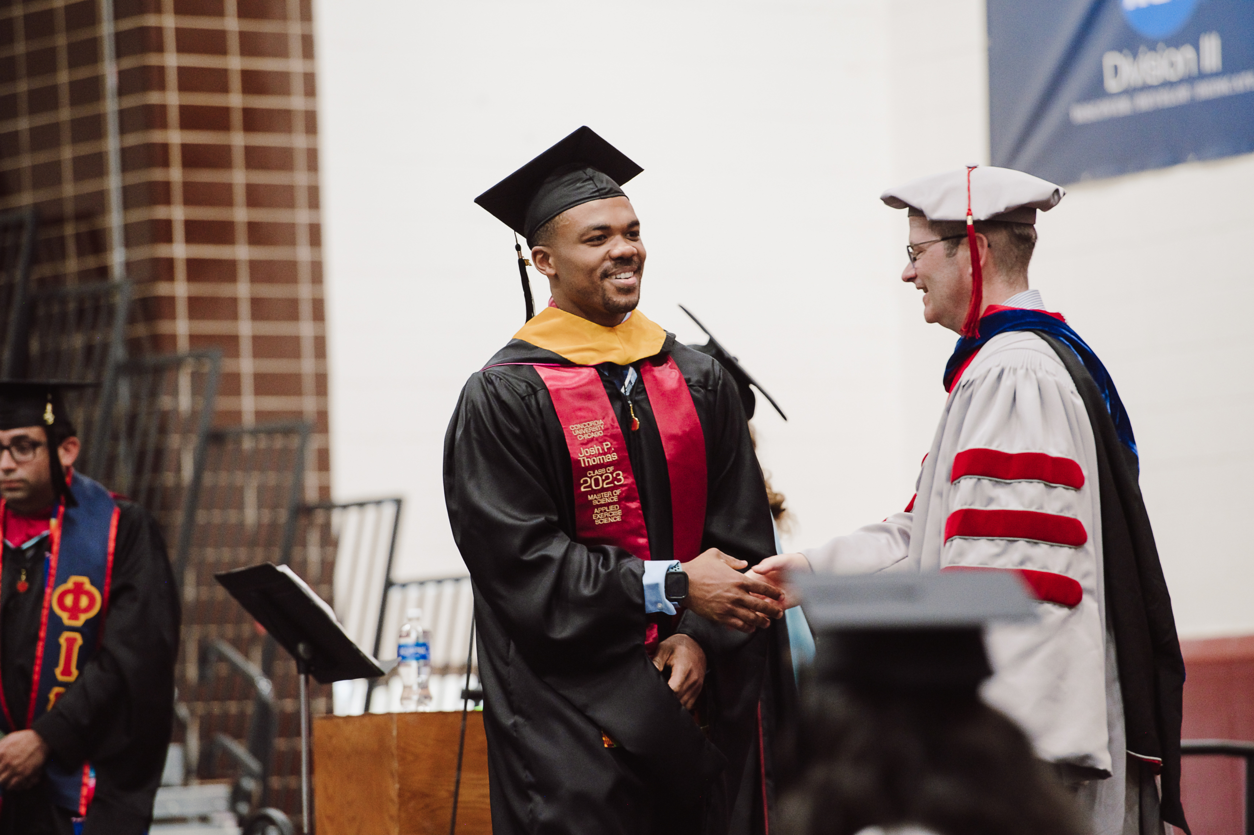 Graduate in cap and gown shaking hands at commencement ceremony after earning degree.